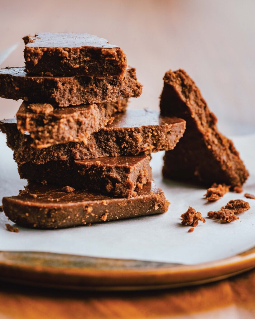 A stack of chocolate brownies on a wooden plate with parchment paper.