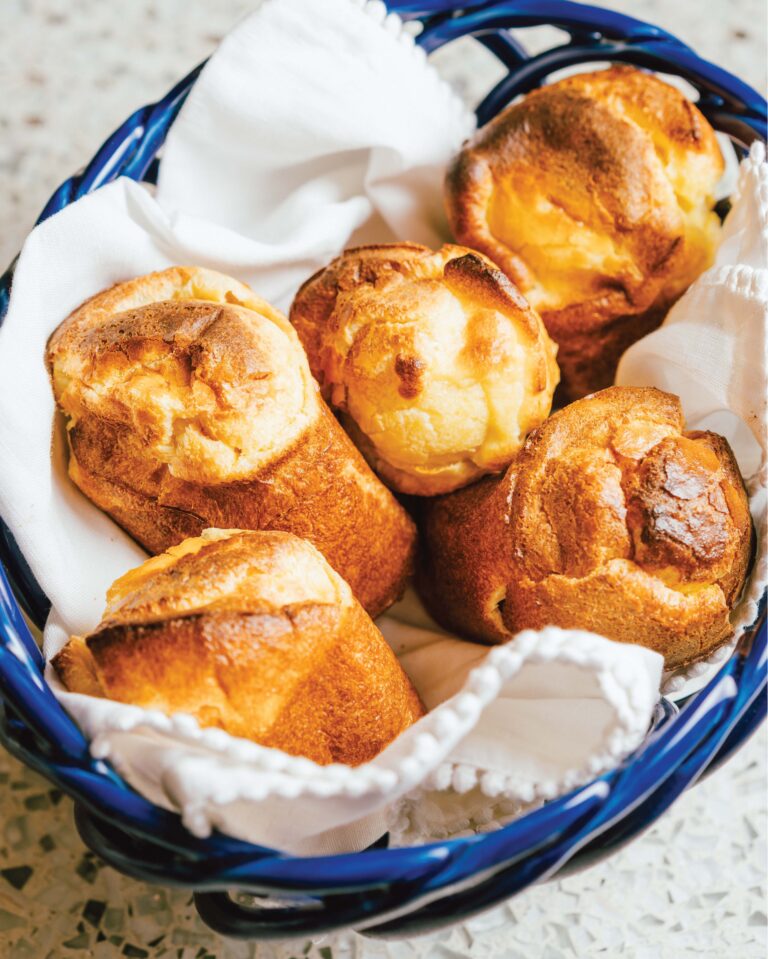 A basket of golden-brown popovers on a white cloth in a blue basket.