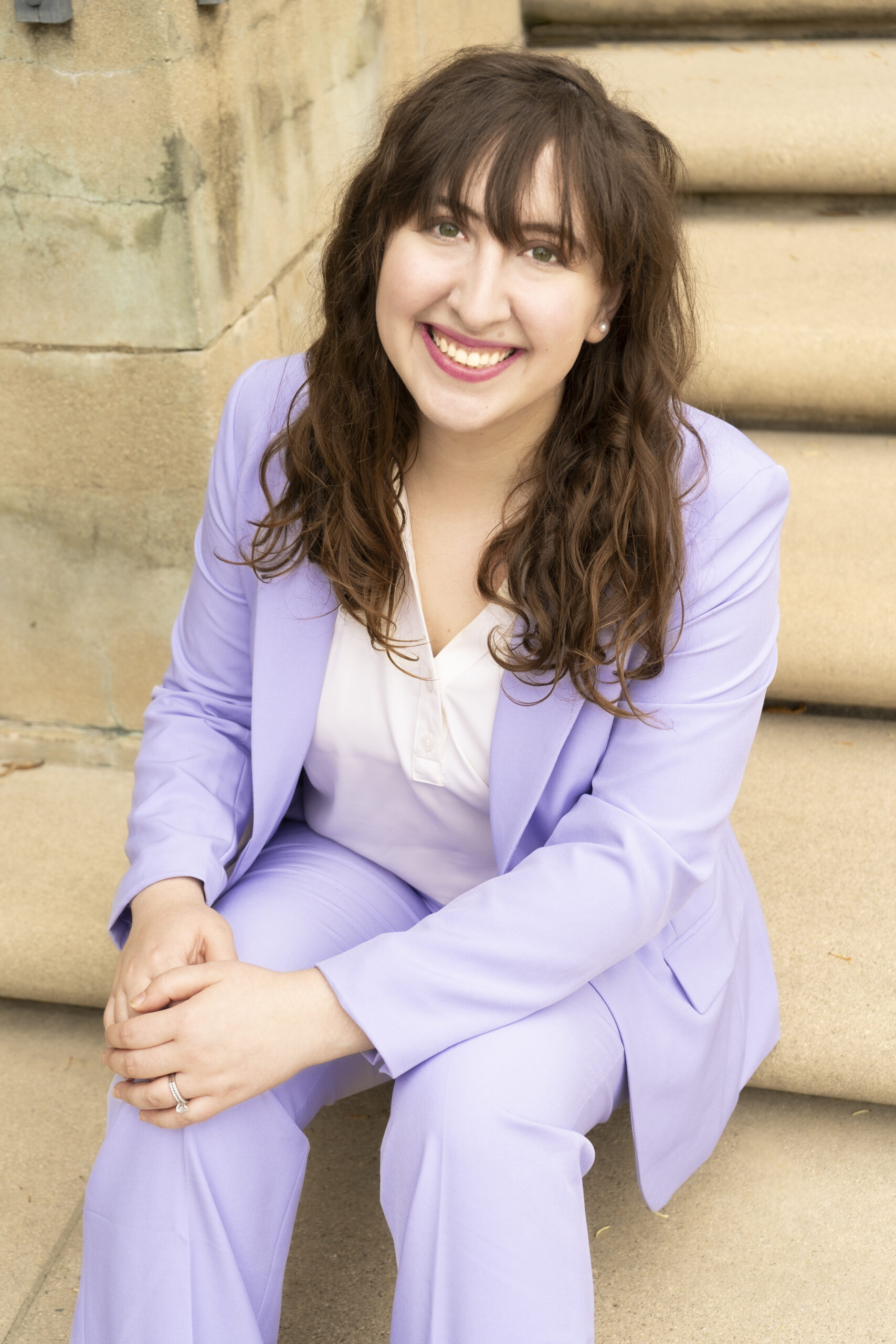 Woman in a light purple suit sitting on steps, smiling at the camera.