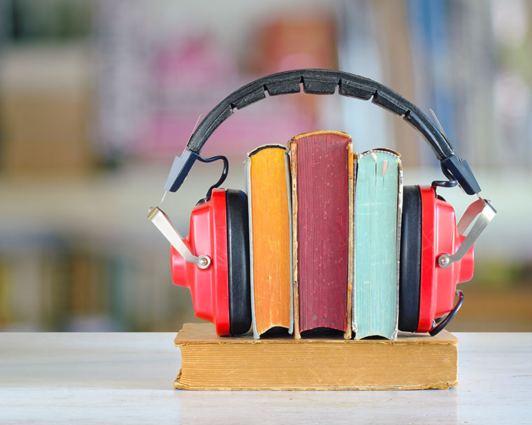 Headphones rest on colorful books, symbolizing audiobooks, with a blurred library background.