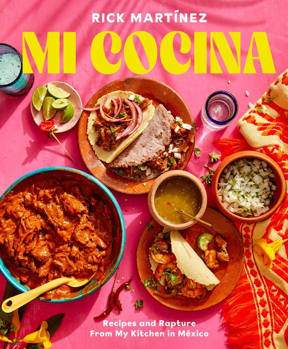Cover of "Mi Cocina" cookbook with vibrant Mexican dishes, tortillas, lime, and drinks on a pink table.