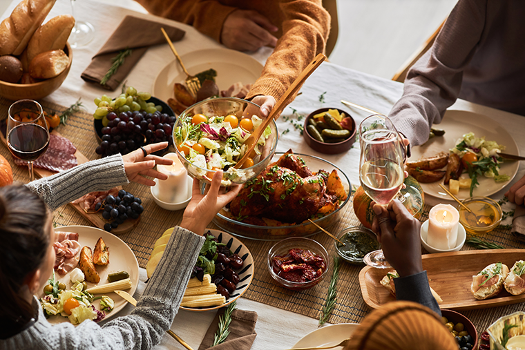 People gathered around a table sharing a meal with salad, roast chicken, and wine during their cookbook club evening.
