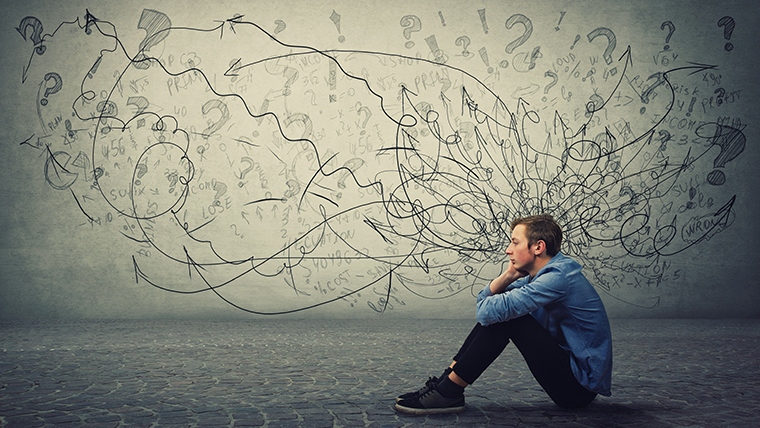 A person sits on the ground with chaotic scribbles and question marks swirling around their head.