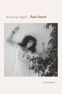 Black-and-white photo of a woman in a white dress with arms raised beside leafy branches; text reads “Bread of Angels”.