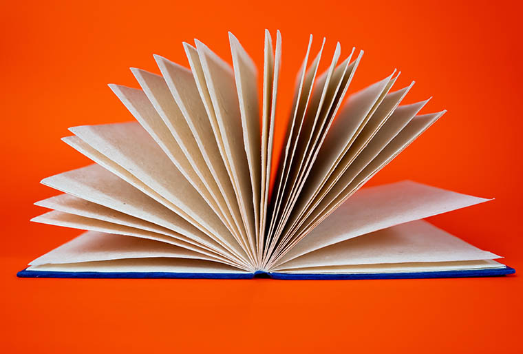 An open book with blank pages fanned out against a bright orange background.
