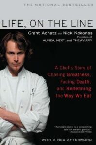 Chef in white coat stands with arms crossed on the cover of “Life, on the Line” book by Grant Achatz.