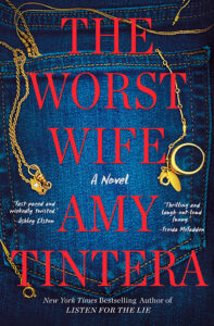A gold necklace and ring on blue jeans with the book title “The Worst Wife” by Amy Tintera in red text.