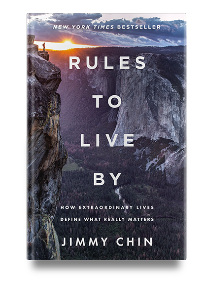 Book cover of “Rules to Live By” by Jimmy Chin, featuring a person standing on a cliff overlooking a mountain valley.